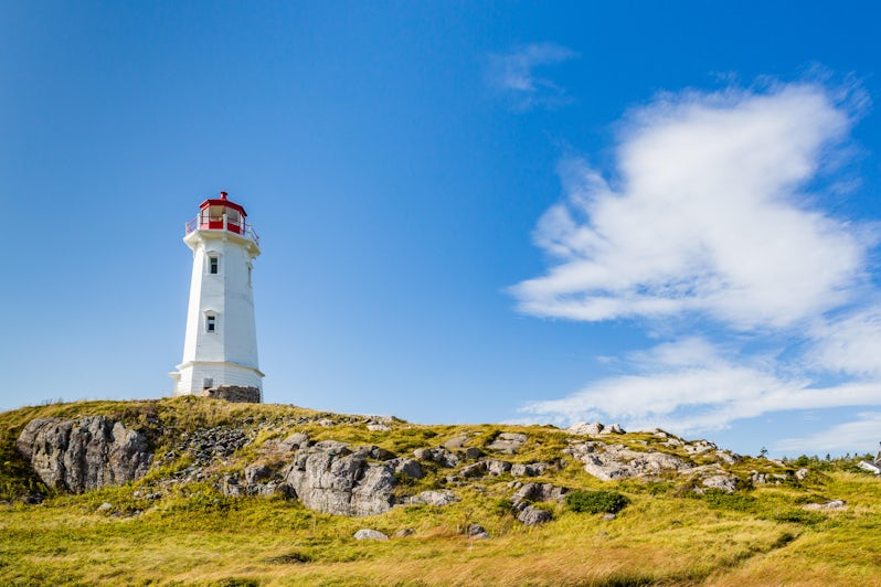 Lush green landscape, blue skies and a red-tipped lighthouse on the coast of Sydney, Nova Scotia