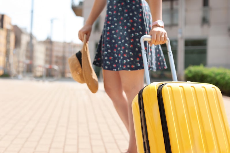 Young woman with yellow carry-on suitcase outdoors