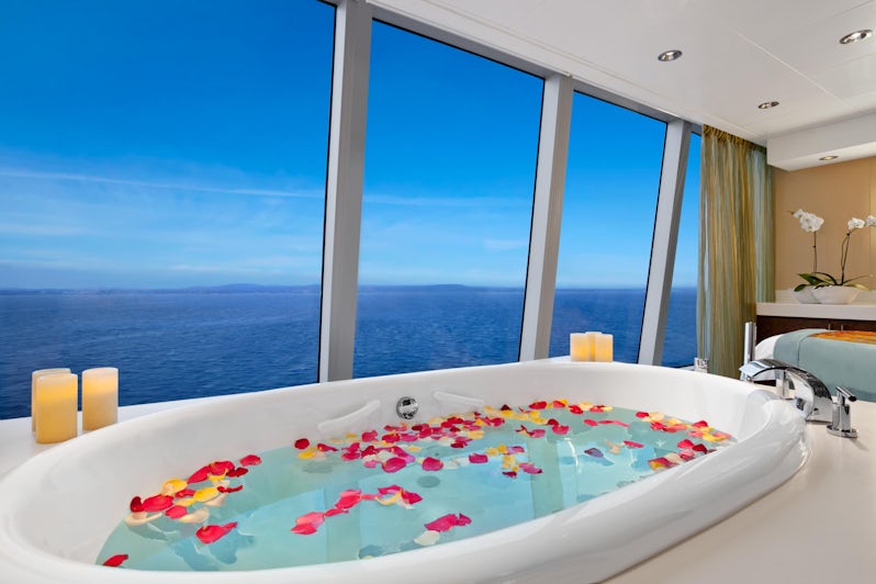 A bath tub filled with water and rose petals overlooking the ocean inside the Aquamar Spa