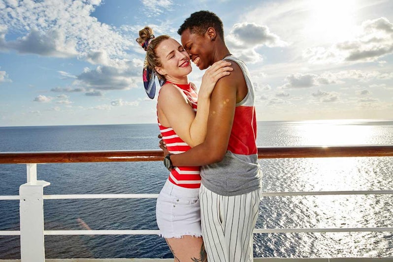 A bi-racial lesbian couple smiling and hugging on a cruise ship deck