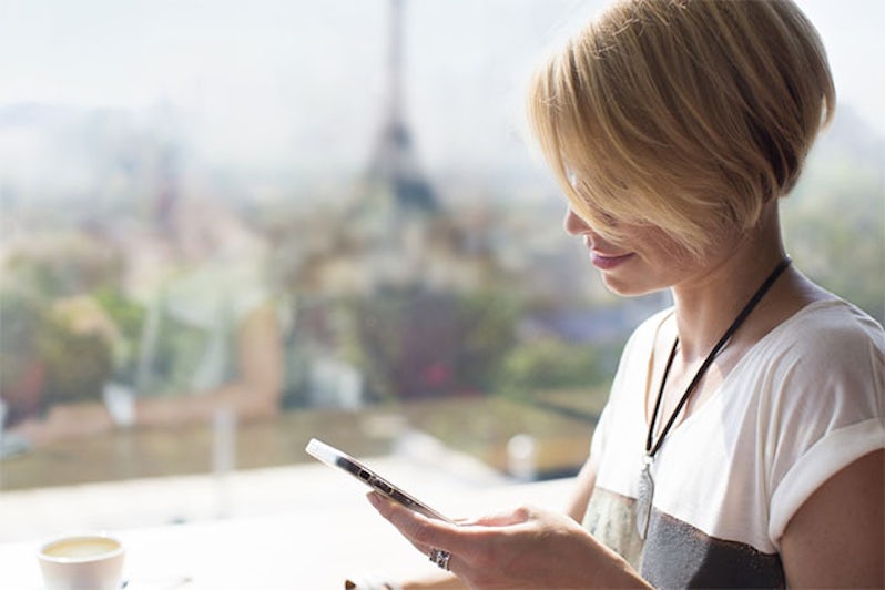 Girl using phone in a Parisian cafe with Eiffel Tower in the background
