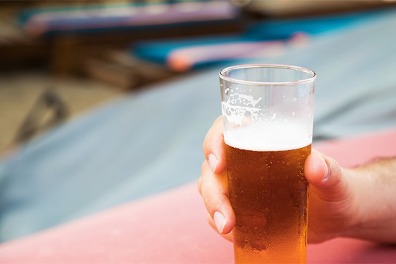 Closeup of a male hand holding a glass of beer on the beach.