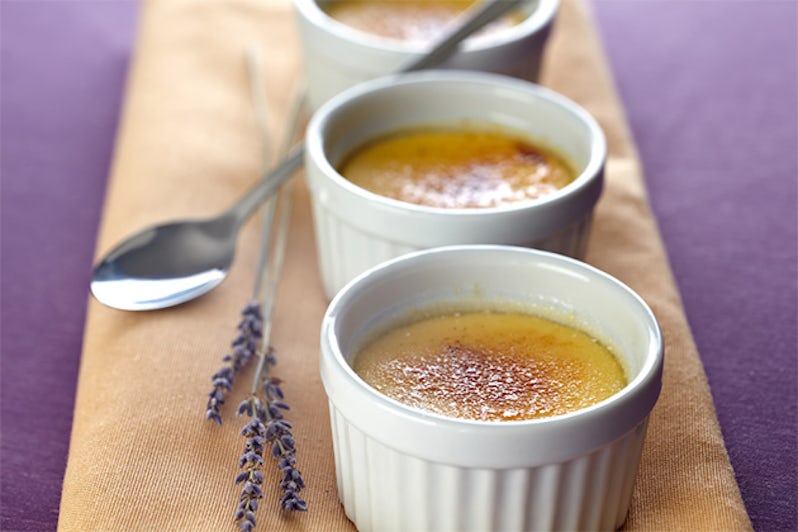 Creme Brulee in three little baking molds on a beige napkin placed on a violet tablecloth. Decorated with lavender blossoms. violet lavender blooms. Shallow depth of field