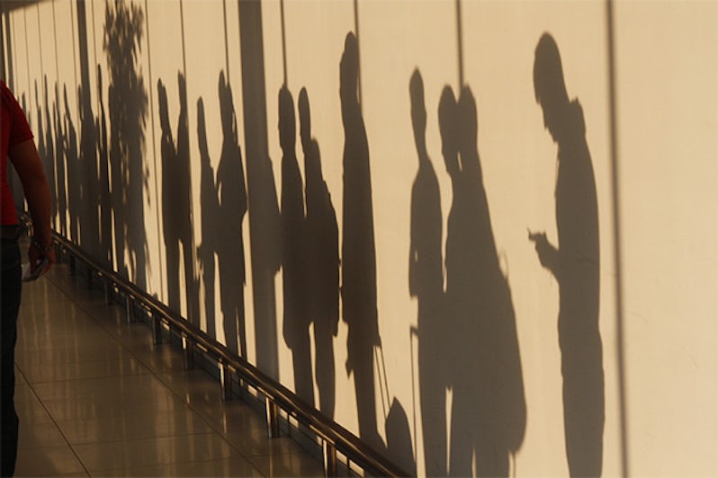Shadows of people waiting in line talking and checking smartphones.