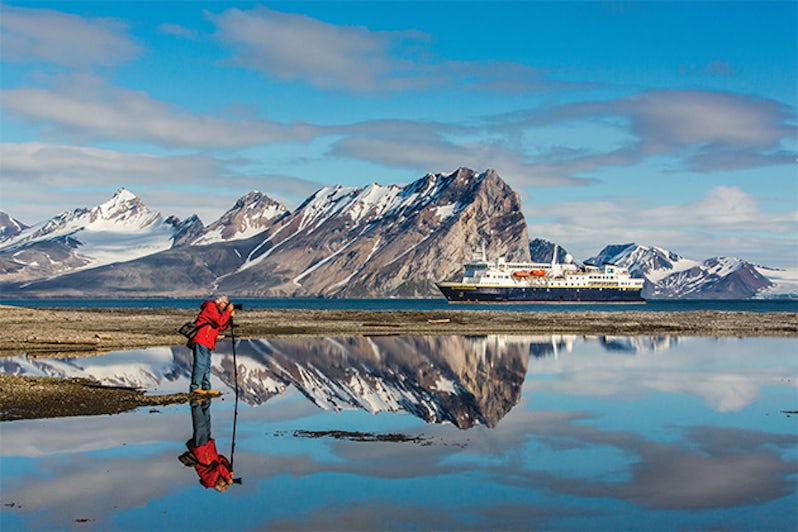 Man photographing Arctic landscape with National Geographic Explorer and mountainous landscape in the background