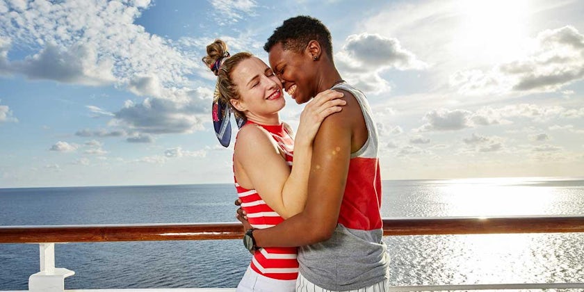 A bi-racial lesbian couple smiling and hugging on a cruise ship deck