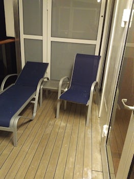 Balcony at night with outside light on showing 2 lounge chairs and table.