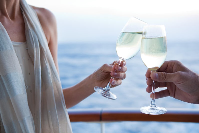 Close-up image of a man and woman toasting their Champagne glasses on a cruise ship deck, with ocean in the background