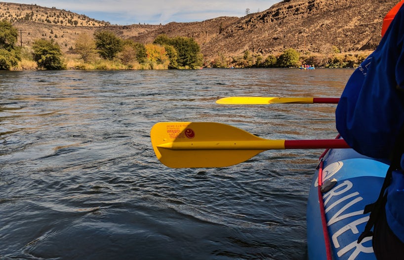 A raft full of people in the background with yellow oars and part of a raft in the foreground. (Photo: John Roberts)