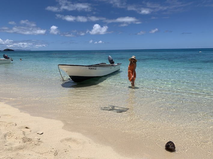 A woman stands in the water next to a fishing boat in Druvani, Fiji