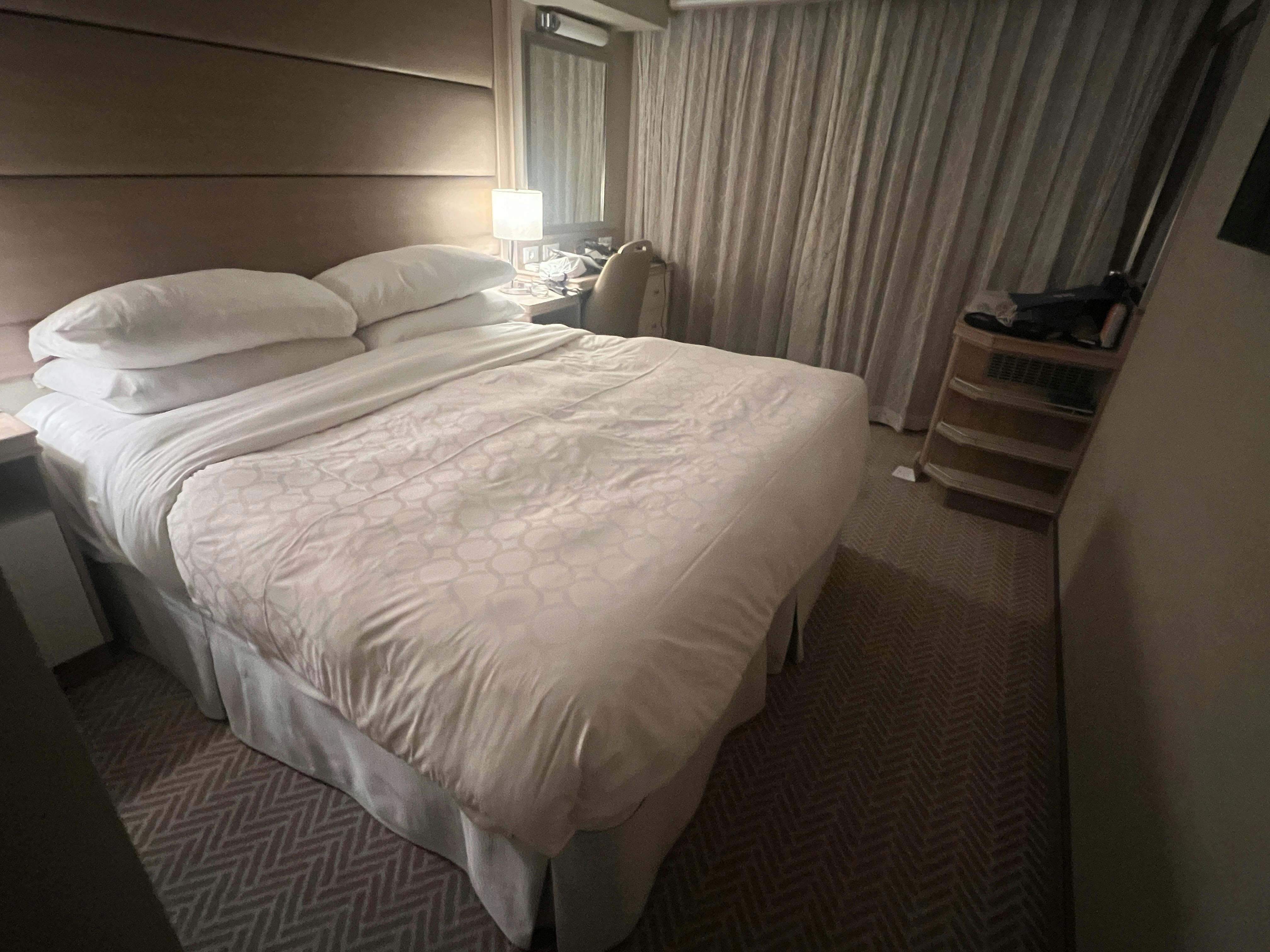 A cozy cruise room with a neatly made double bed, soft lighting, bedside table with a lamp, and thick curtains covering the window.