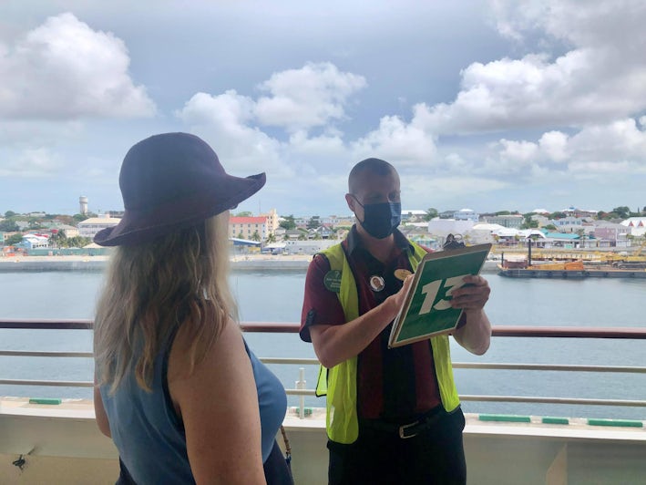 A woman does her e-muster drill while a man holding a clipboard talks on Adventure of the Seas