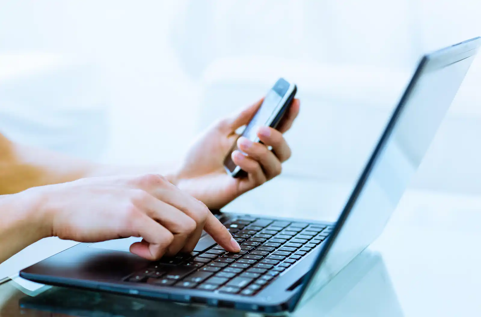 Woman typing on computer and consulting her cell phone for travel plans
