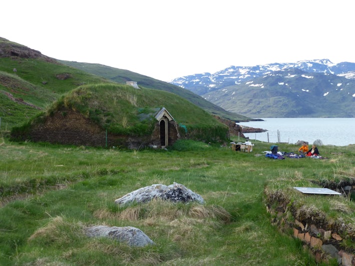 Travelers relax near one of the Reconstructed Viking Buildings at Brattahlid in Qassiarsuk, Greenland (Photo: Sarah Schlichter/Shutterstock)