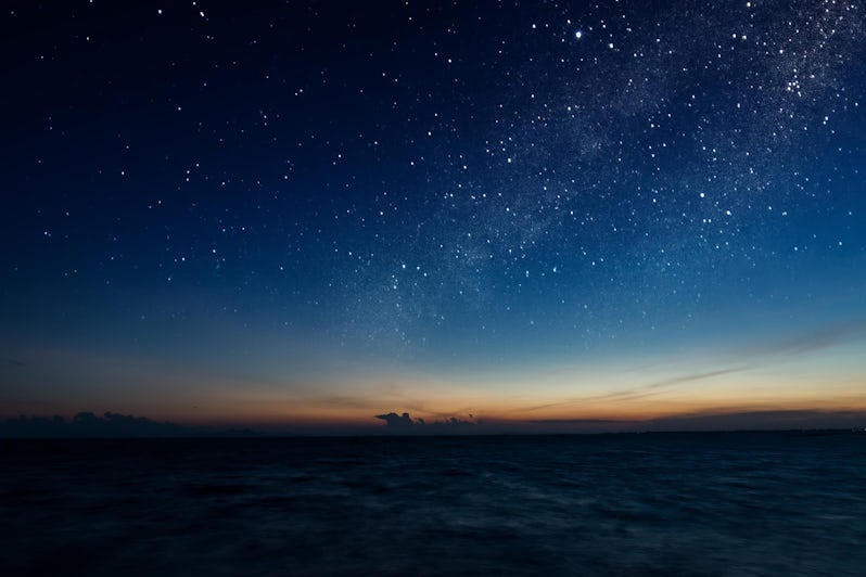 A starry night sky emerges during dusk at sea
