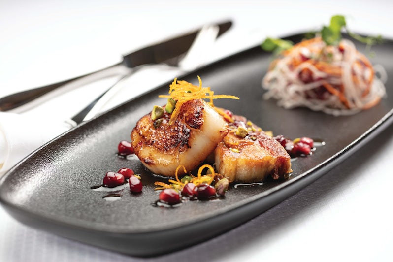 Close-up shot of plated seared diver scallops with cured pork belly confit and pomegranate seeds