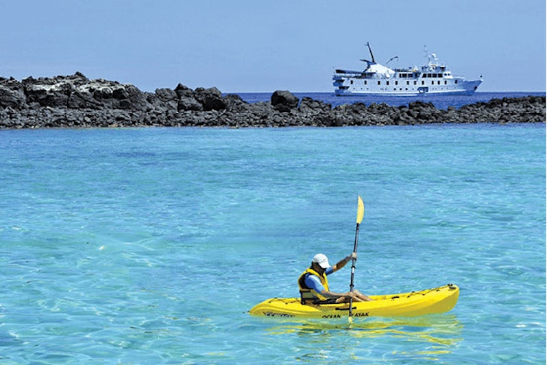 Man kayaking in crystal blue waters with La Pinta ship in the background