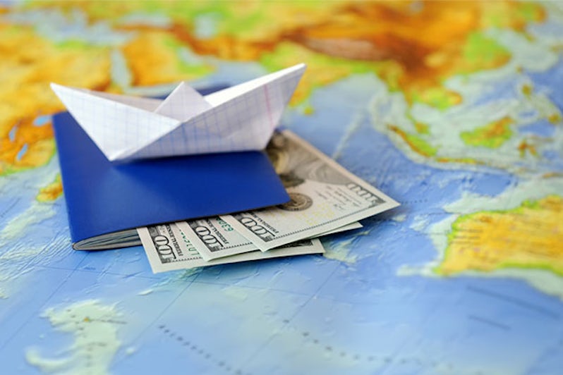 Paper boat with passport and $300 placed on top of a world map