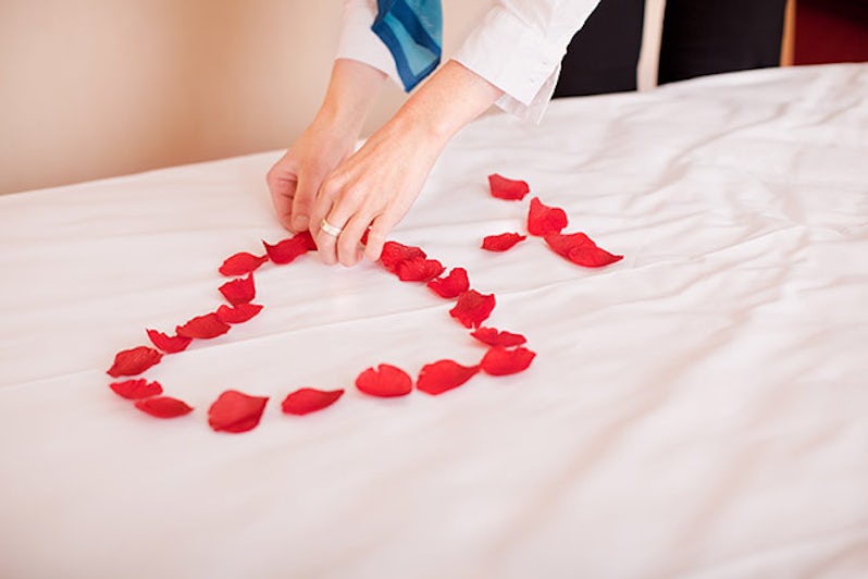 Hands arranging petals in heart shape on bed