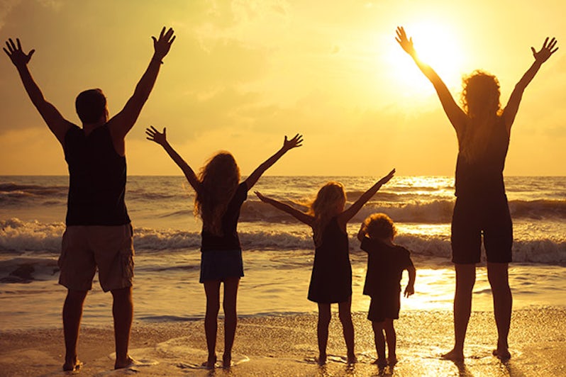 Happy family standing on the beach at sunset