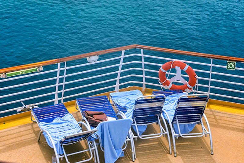 Lounge chairs on deck of cruise ship with towels on them in sunny caribbean