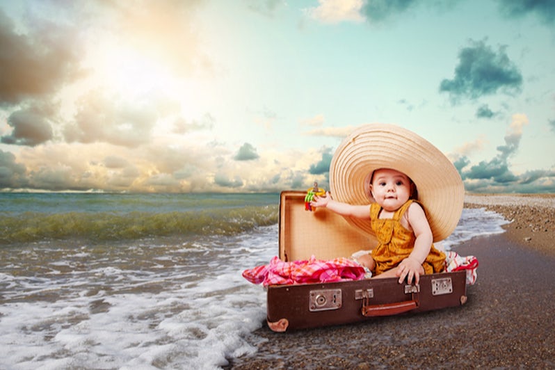 Funny baby girl traveler sitting in retro suitcase