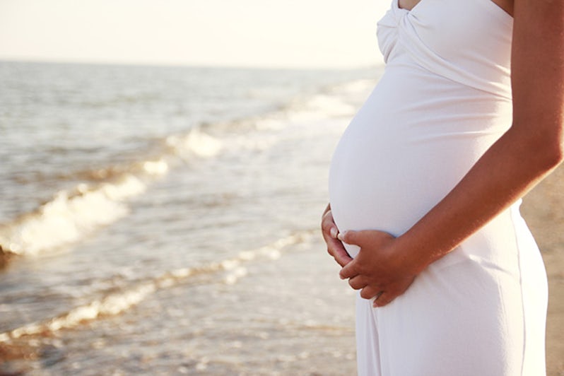 Profile shot of a woman's pregnant belly, with beach in the backgroun