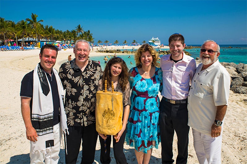 Family posing with the Torah on a Caribbean beach with Destination Mitzvah chartered ship in the background