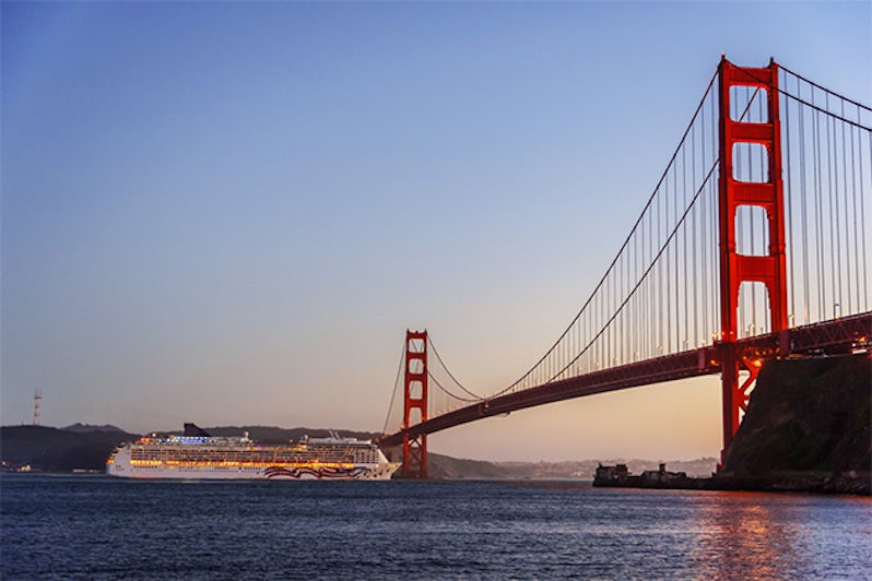 A white cruise ship passing under the Golden Gate Bridge in San Francisco at dusk.