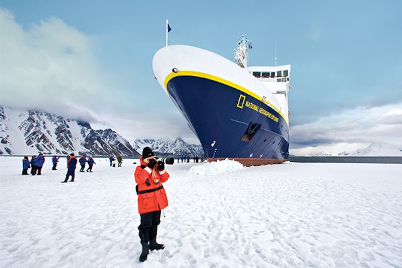 Passenger photographing Antarctica landscape with National Geographic Explorer docked in the background