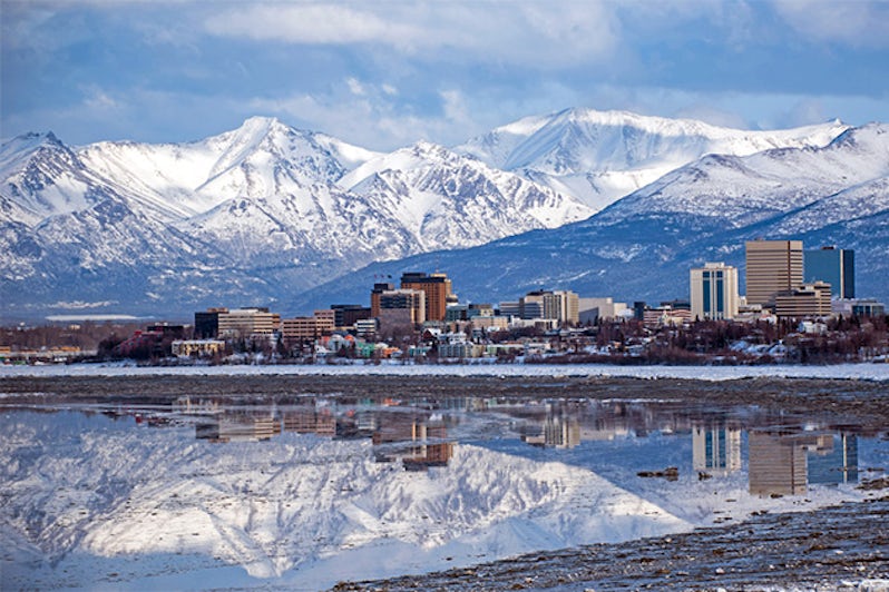 Anchorage city skyline, with reflection of towering, snowy mountains in the water below