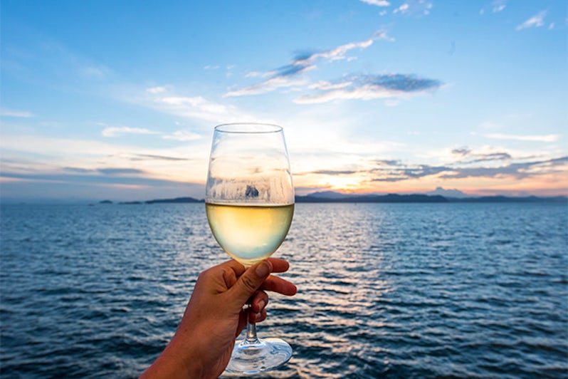 Woman holding glass of wine, with sea and sunset in the background