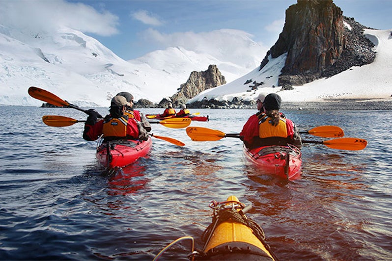 Three kayakers with Antarctic backdrop