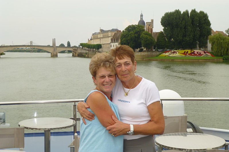 Two mature women hugging on river boat with bridge in background