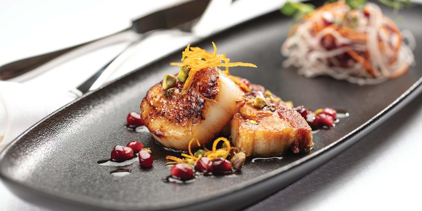 Close-up shot of plated seared diver scallops with cured pork belly confit and pomegranate seeds