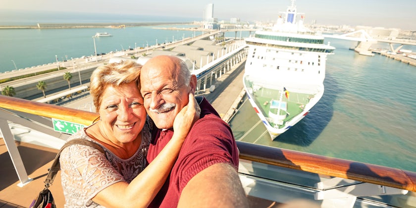 Senior couple taking a selfie in front of their cruise ship docked in port