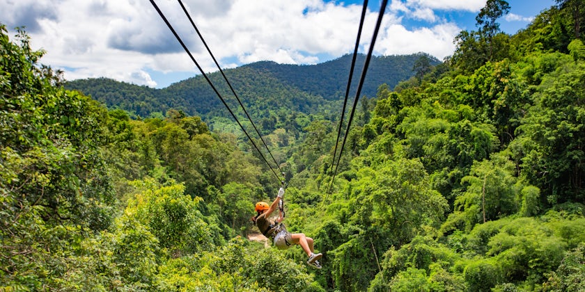 Woman in orange helmet ziplining through a lush forest in Chiang Mai, Thailand