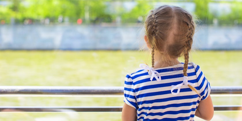 Little girl with braids looking out towards the water on the balcony of a river cruise ship