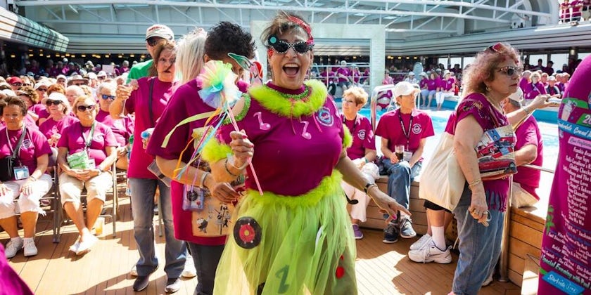 Female passenger dressed in a pink and green costume, smiling, onboard The Malt Shop Memories Cruise