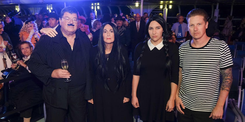 Four people dressed up as the Addams Family, looking into the camera and not smiling