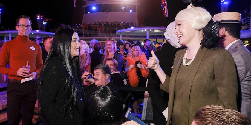 Passenger dressed up as Morticia Addams, smiling and interacting with TCM host Alicia Malone onboard the TCM Cruise at a costume party