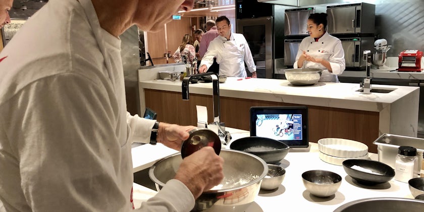 Shot of a passenger mixing a bowl of ingredients at Culinary Kitchen, with chef instructors in the background