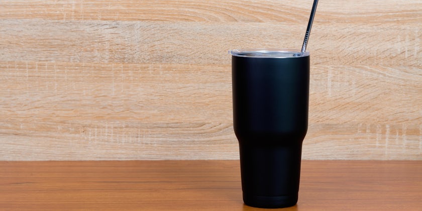 Black color stainless steel tumbler or cold storage cup with water straw and cap on wooden background.