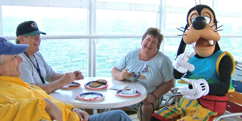 Group of smiling adults dining with Goofy on the lido deck on Disney Cruise Line