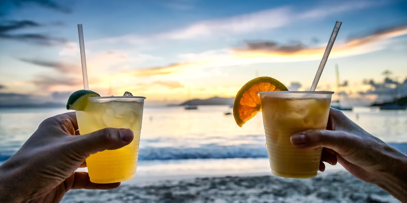 Toasting with tropical drinks at sunset with island beach background; focus on drinks