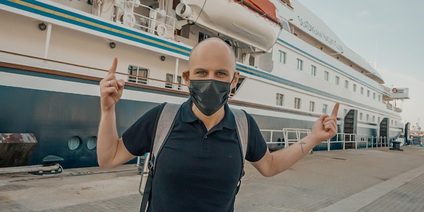 Passenger wearing a mask and posing for a photo in front of SeaDream I before a cruise