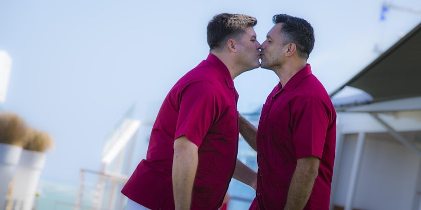 A same-sex male couple kissing in matching outfits before their wedding on Celebrity Cruises
