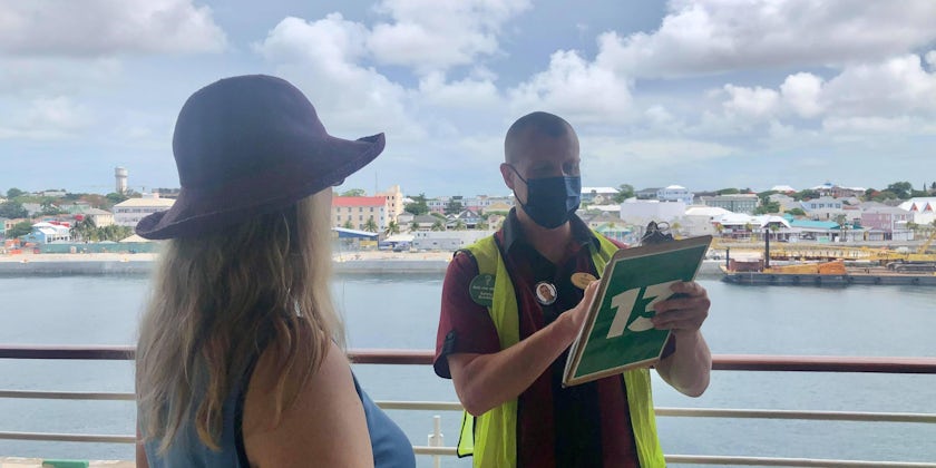 A woman does her e-muster drill while a man holding a clipboard talks on Adventure of the Seas