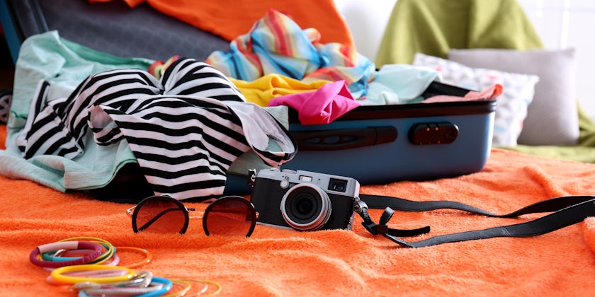 Open suitcase with vacation clothes, sunglasses and a camera