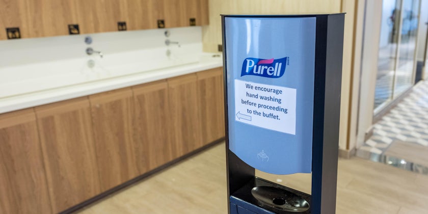 Purell hand sanitizer with sinks in the background, and sign encouraging passengers to wash their hands (Photo: Cruise Critic)